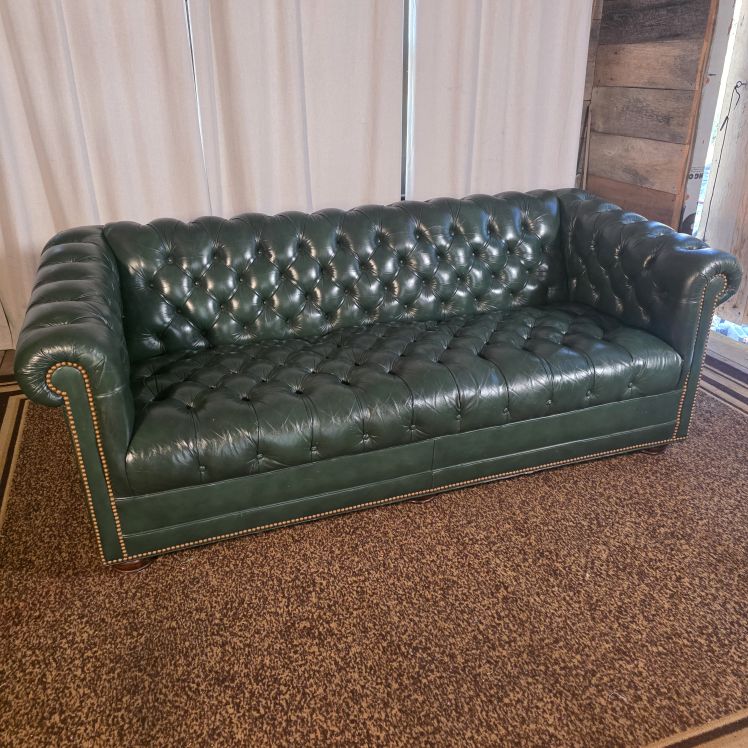 Front view of green leather Chesterfield sofa with deep button tufting, rolled arms, and nailhead trim