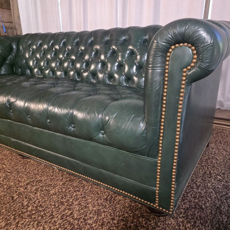Angled view of green leather Chesterfield sofa showing rolled arm and nailhead trim