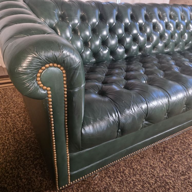 Close-up of rolled arm with nailhead trim and tufted seat on green leather Chesterfield sofa